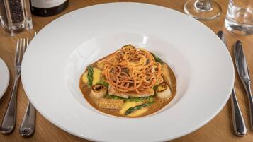Un plato blanco con un guiso de fideos, verduras y salsa sobre una mesa de madera.