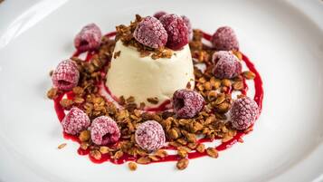 Un dessert servi dans une assiette blanche, garni de framboises et de granola.