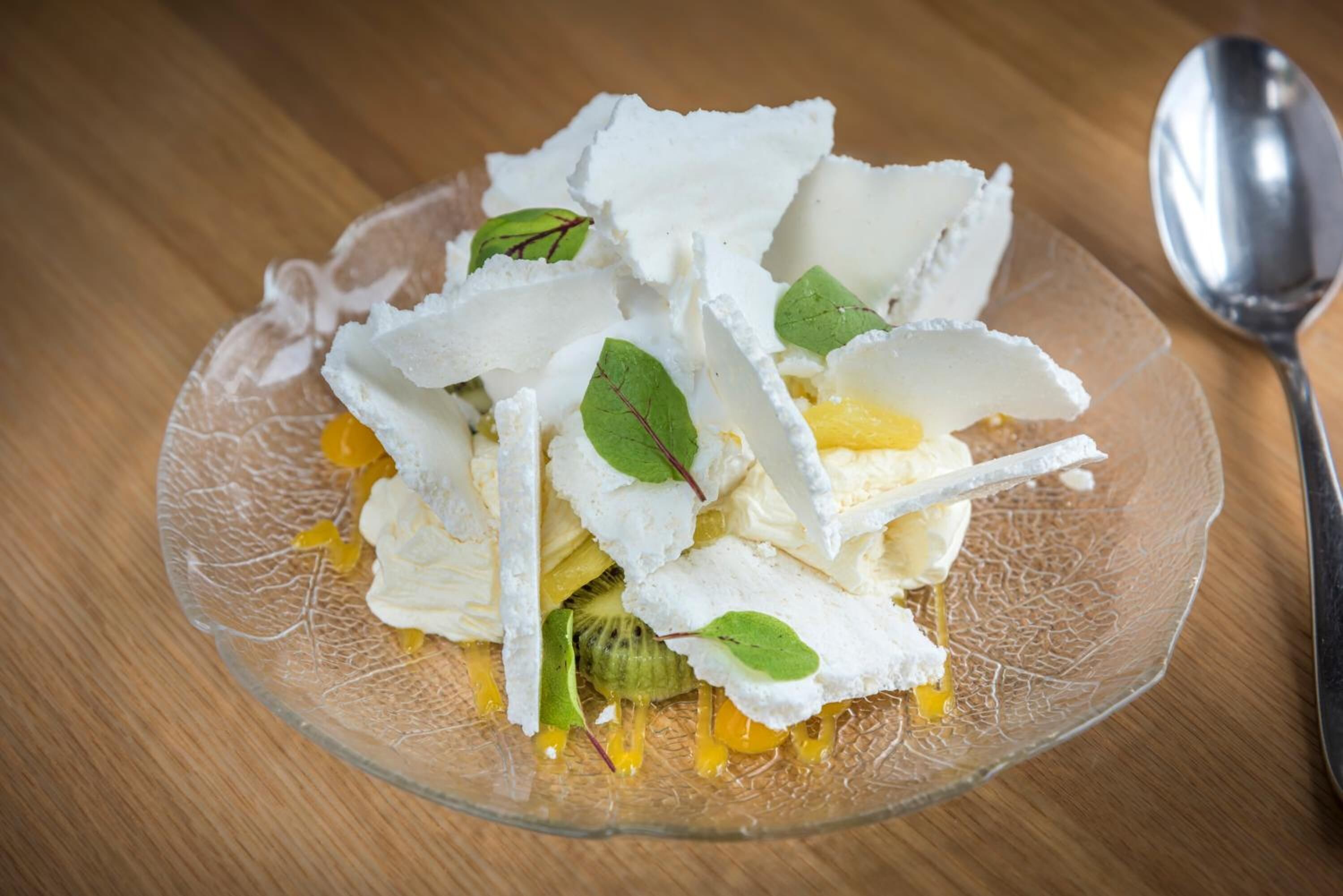 Un postre en una fuente de vidrio transparente con detalles blancos y amarillos, posiblemente comida, sobre una mesa de madera.