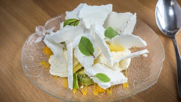 Un postre en una fuente de vidrio transparente con detalles blancos y amarillos, posiblemente comida, sobre una mesa de madera.