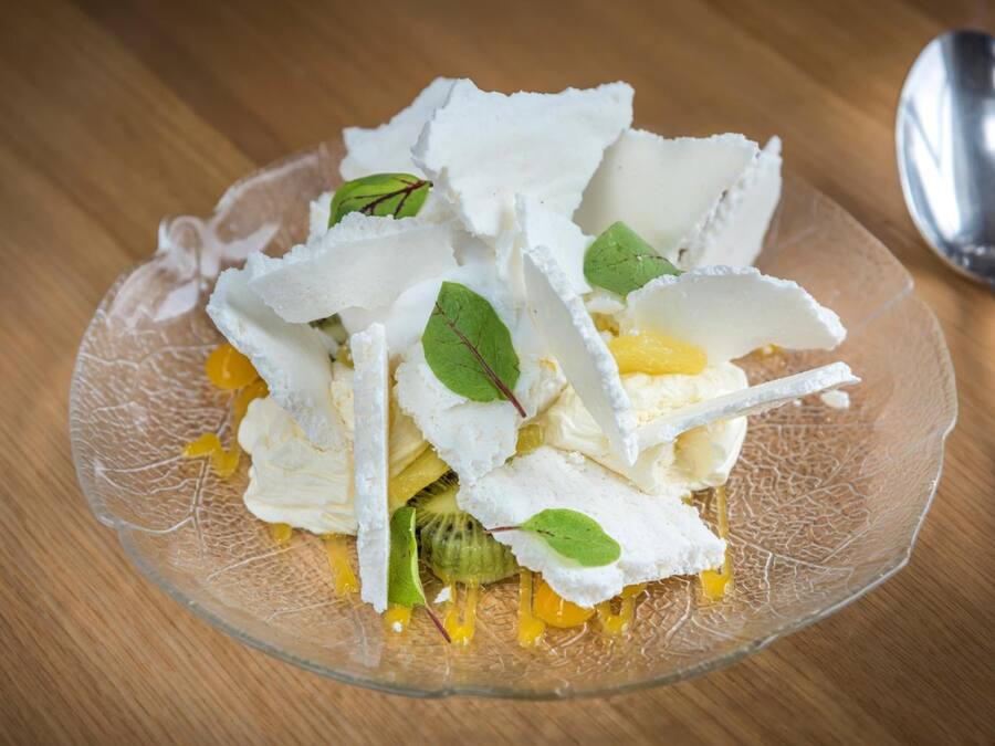 Un postre en una fuente de vidrio transparente con detalles blancos y amarillos, posiblemente comida, sobre una mesa de madera.