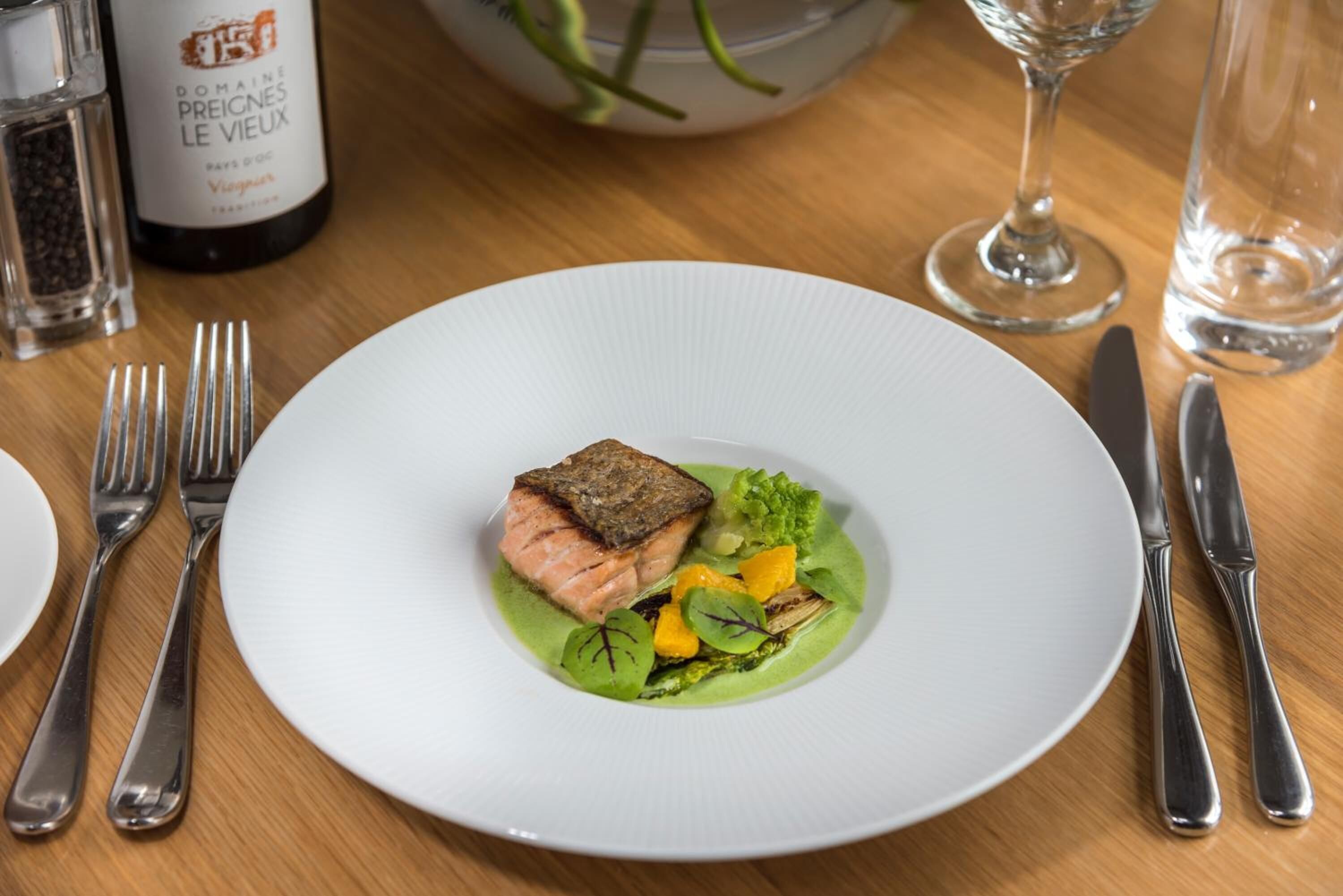 Um prato branco com salmão, aspargos e um molho verde sobre uma mesa de madeira.