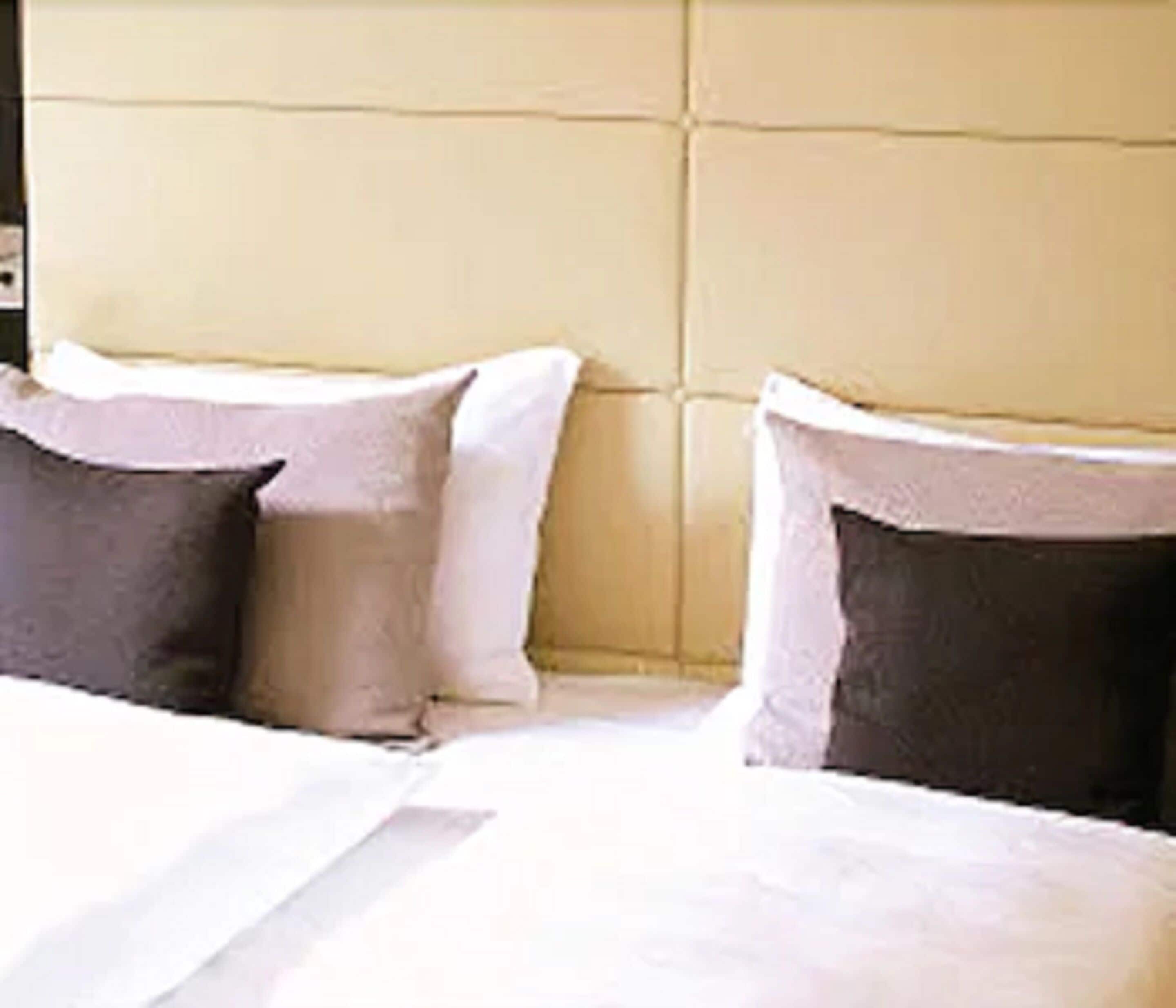 A bed with white bedding and two pillows, one dark and one light.