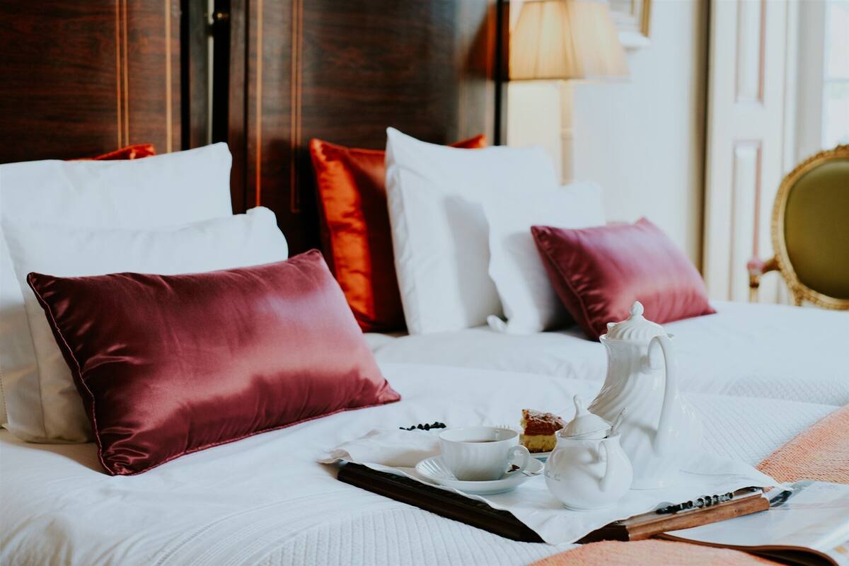 Una cama bien hecha con sábanas blancas, almohadas rojas y blancas, y un juego de té a un lado.