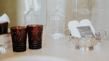 Deux verres de couleur brun foncé, un plateau en argent avec une serviette blanche et un récipient en verre transparent, le tout dans un décor de salle de bain.