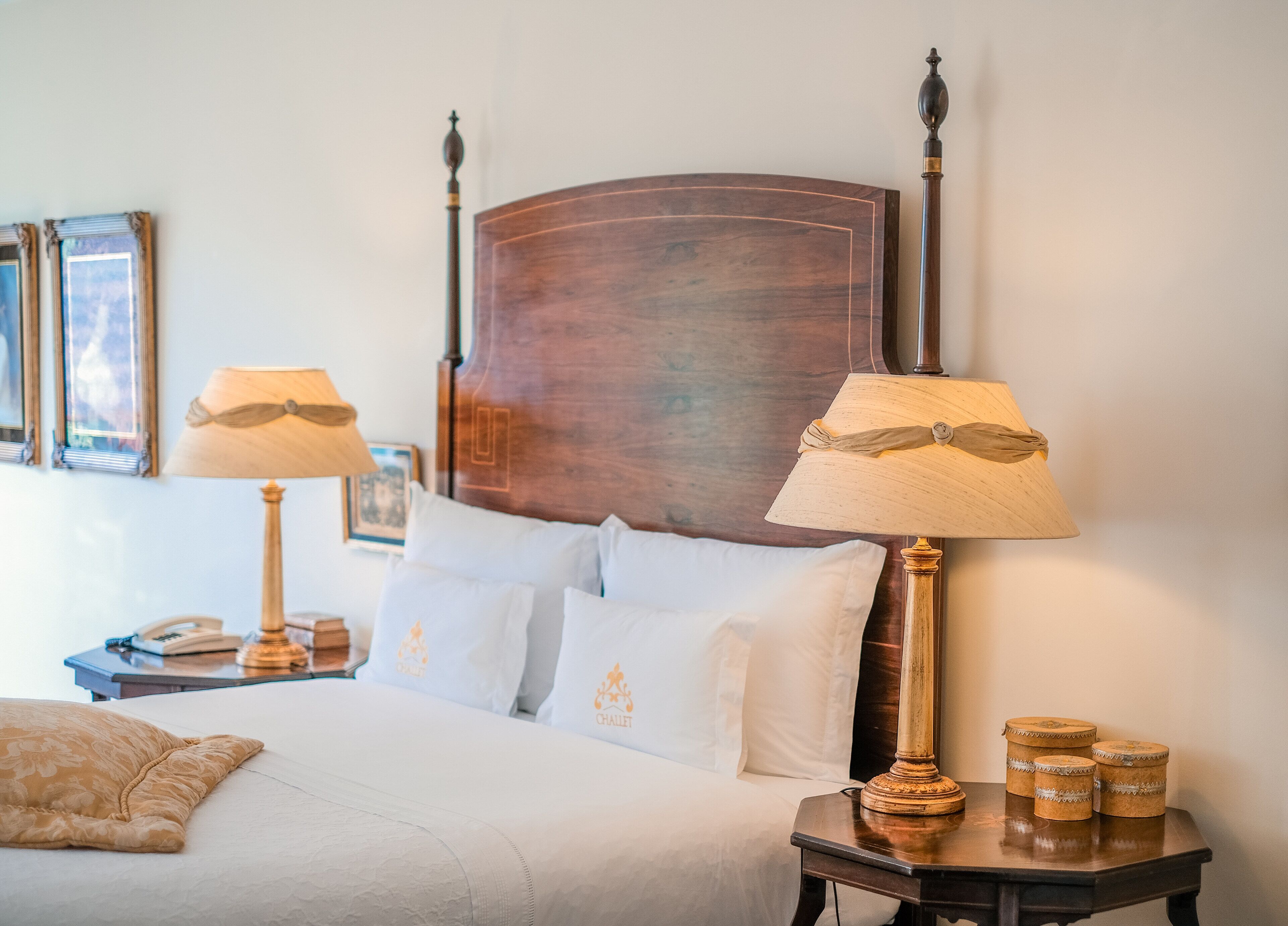A neatly made bed with white linens and two bedside lamps. There are three pillows on the bed, and a small table with a lamp and a decorative item beside it.