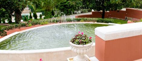 A circular fountain with water jets, surrounded by lush greenery and potted plants.