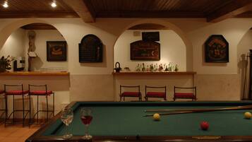 A pool table with billiard balls, a glass of red wine, and a bar area with chairs and bottles.