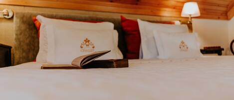 Una cama bien hecha con un libro, almohadas con un logotipo y una lámpara en un techo de madera.