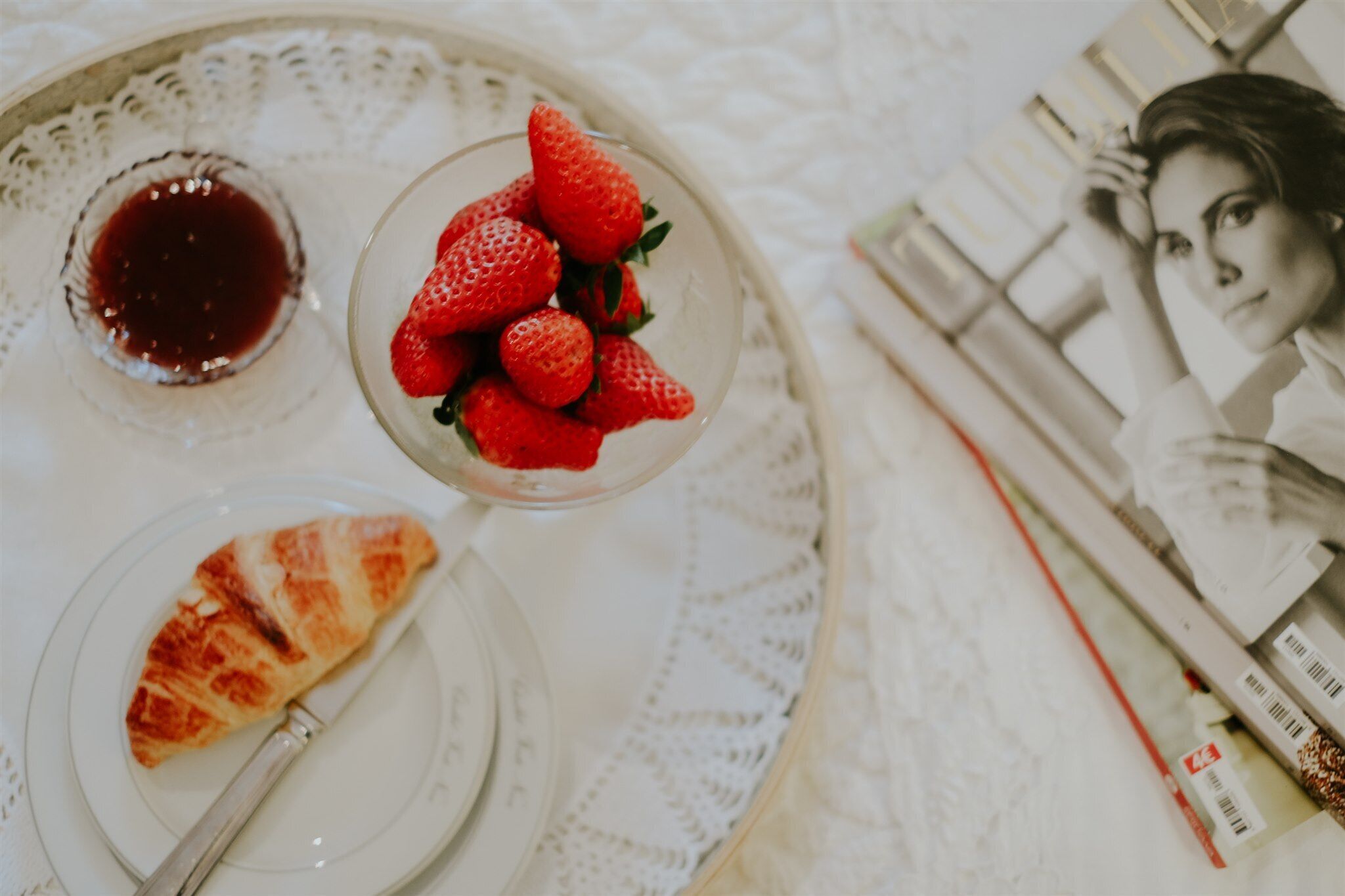 A tray with a croissant, strawberries, and a small bowl of jam.