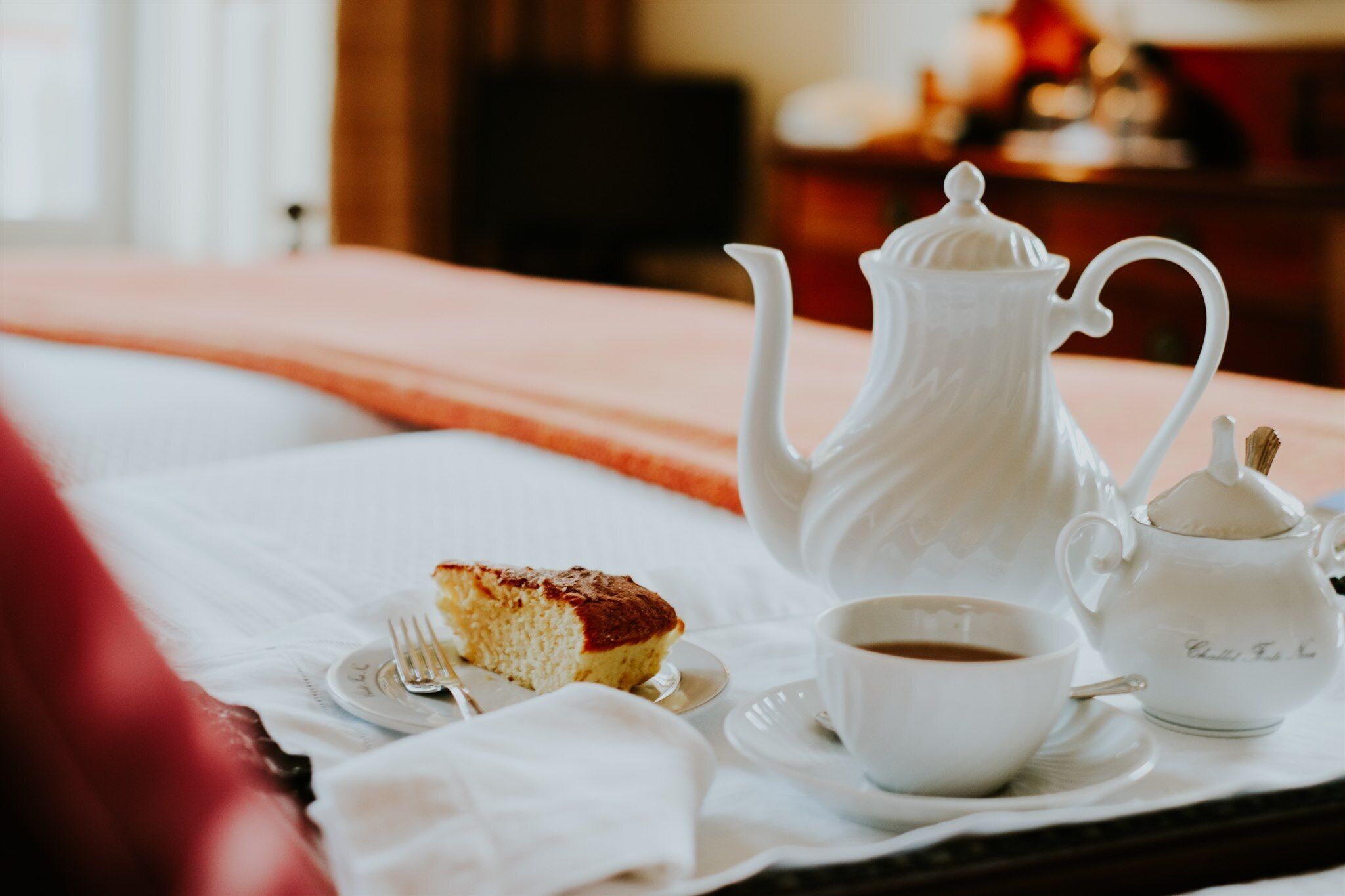 Een ontbijfwagen met een stukje taart, een kop koffie en een theepot op een bed.