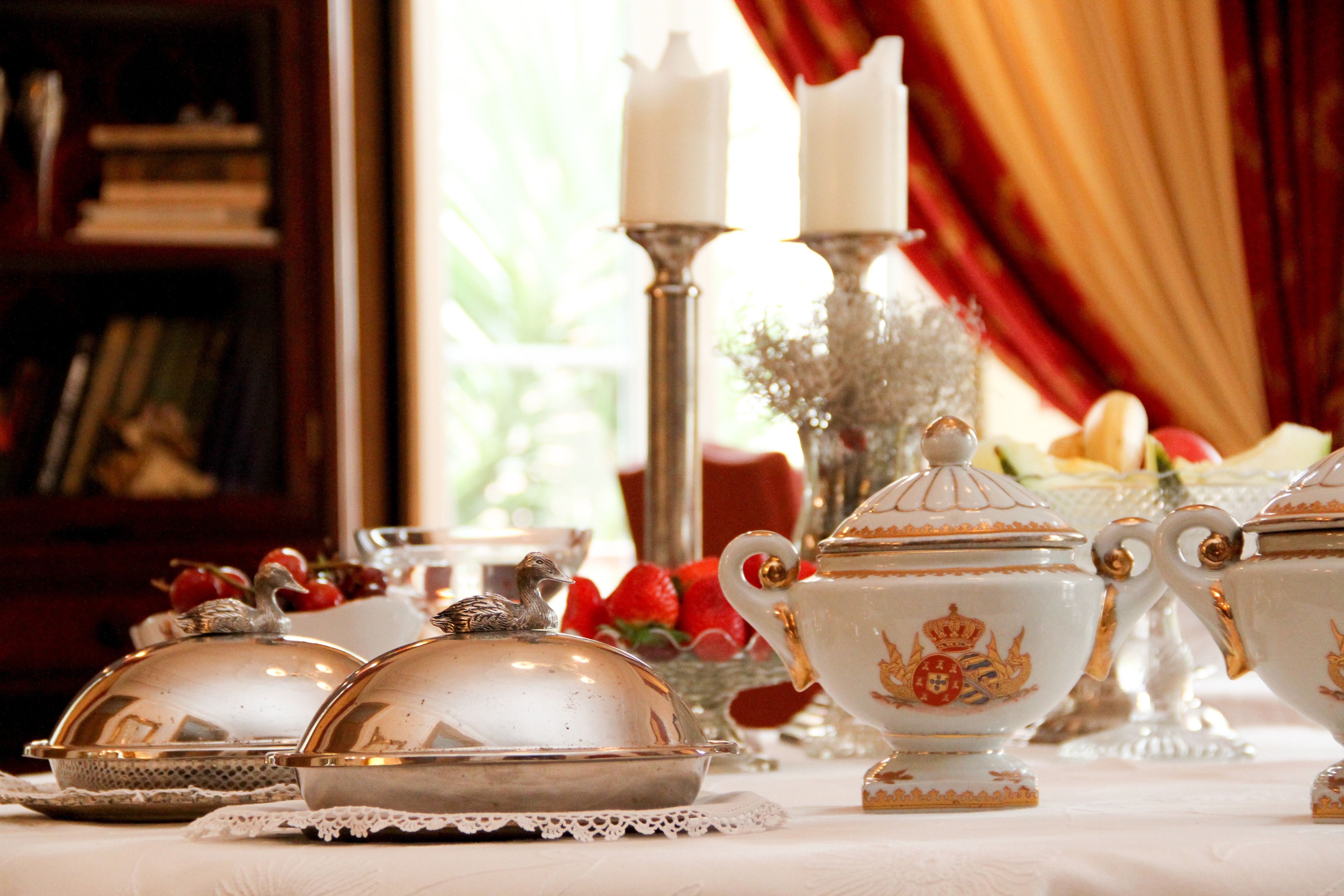 Una mesa dispuesta con vajilla blanca y dorada ornamentada, un candelabro y un florero con flores.