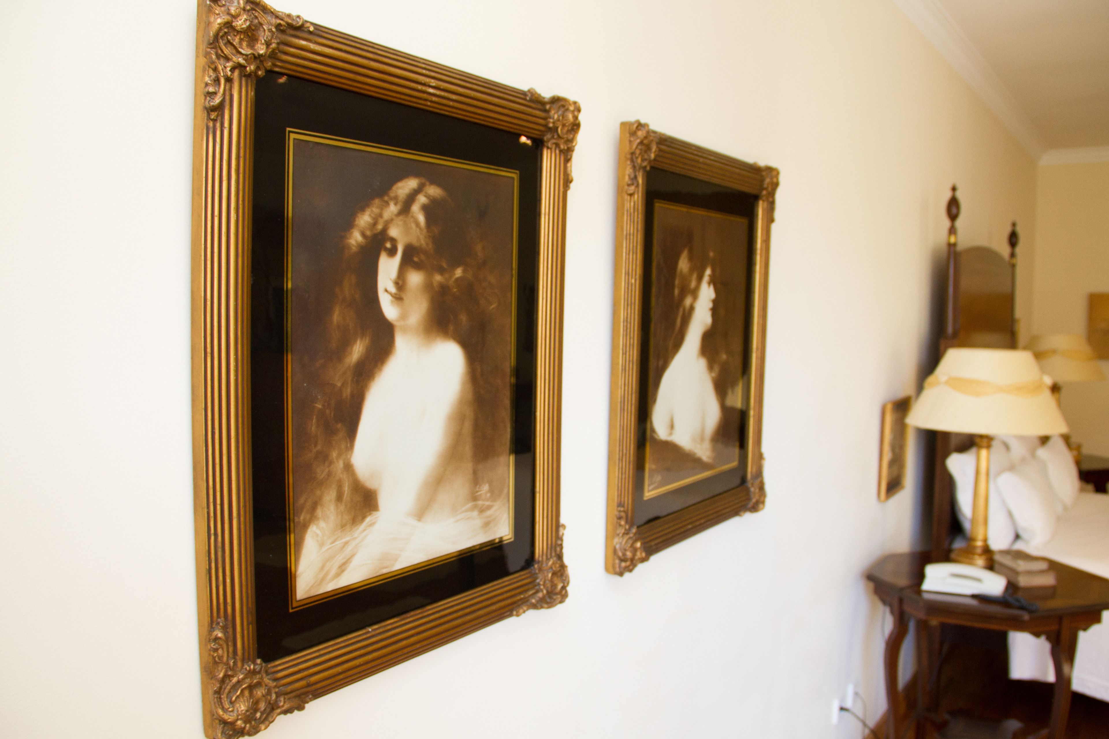 Dos retratos enmarcados en una pared, una lámpara y una mesita de noche con un teléfono.