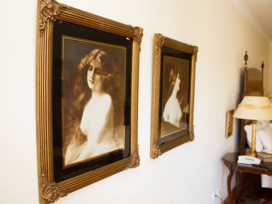 Dos retratos enmarcados en una pared, una lámpara y una mesita de noche con un teléfono.