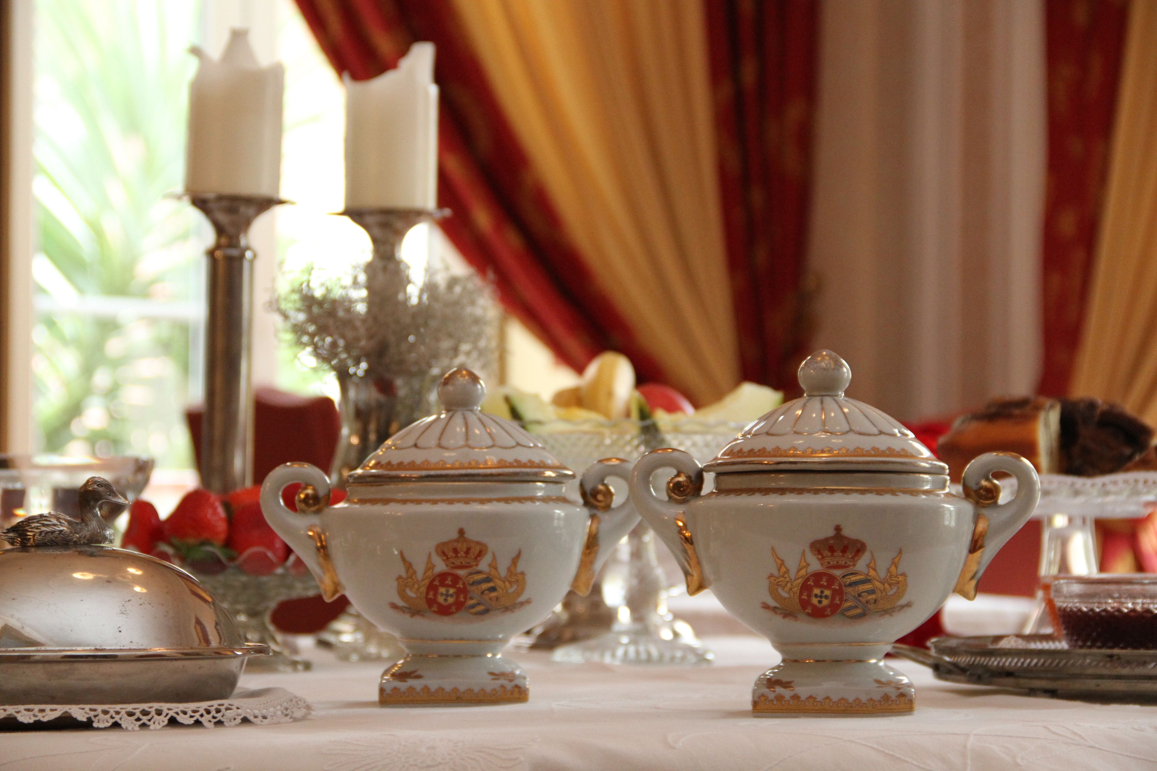 Une table dressée avec des théières blanches décorées de motifs complexes et rehaussées de détails dorés, ainsi qu’un chemin de table en dentelle.