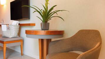 Una habitación moderna con una mesa redonda de madera, un sillón marrón, una planta en maceta, un televisor montado en la pared y una mesita auxiliar con un bolso estampado.