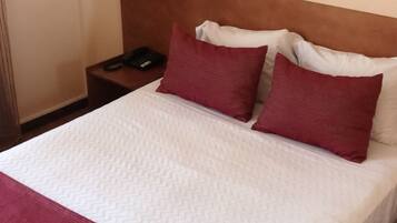 A hotel room with a bed, two red pillows, a white bedspread, and a wooden headboard.
