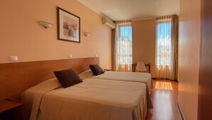 A hotel room with two beds, a desk, a chair, and a window with curtains. - Império Hotel (Peso da Régua)