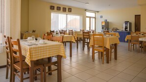 A dining area with multiple tables covered with yellow checkered tablecloths, wooden chairs, and a kitchen area with appliances in the background. - Império Hotel (Peso da Régua)