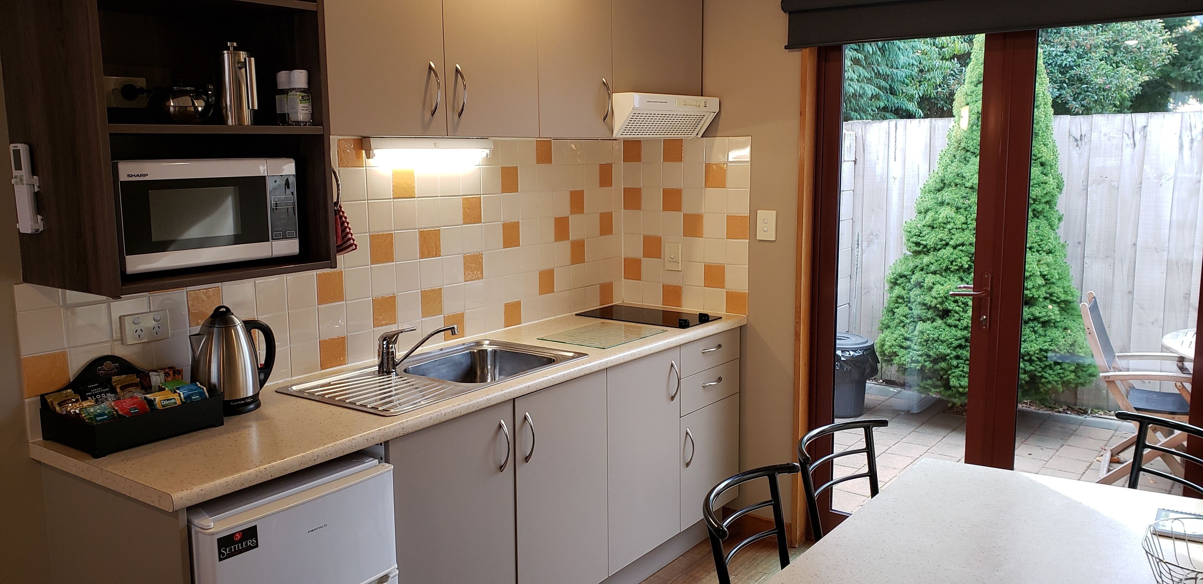 A compact kitchen with a microwave, sink, and a small refrigerator. There is a window providing a view of the backyard.