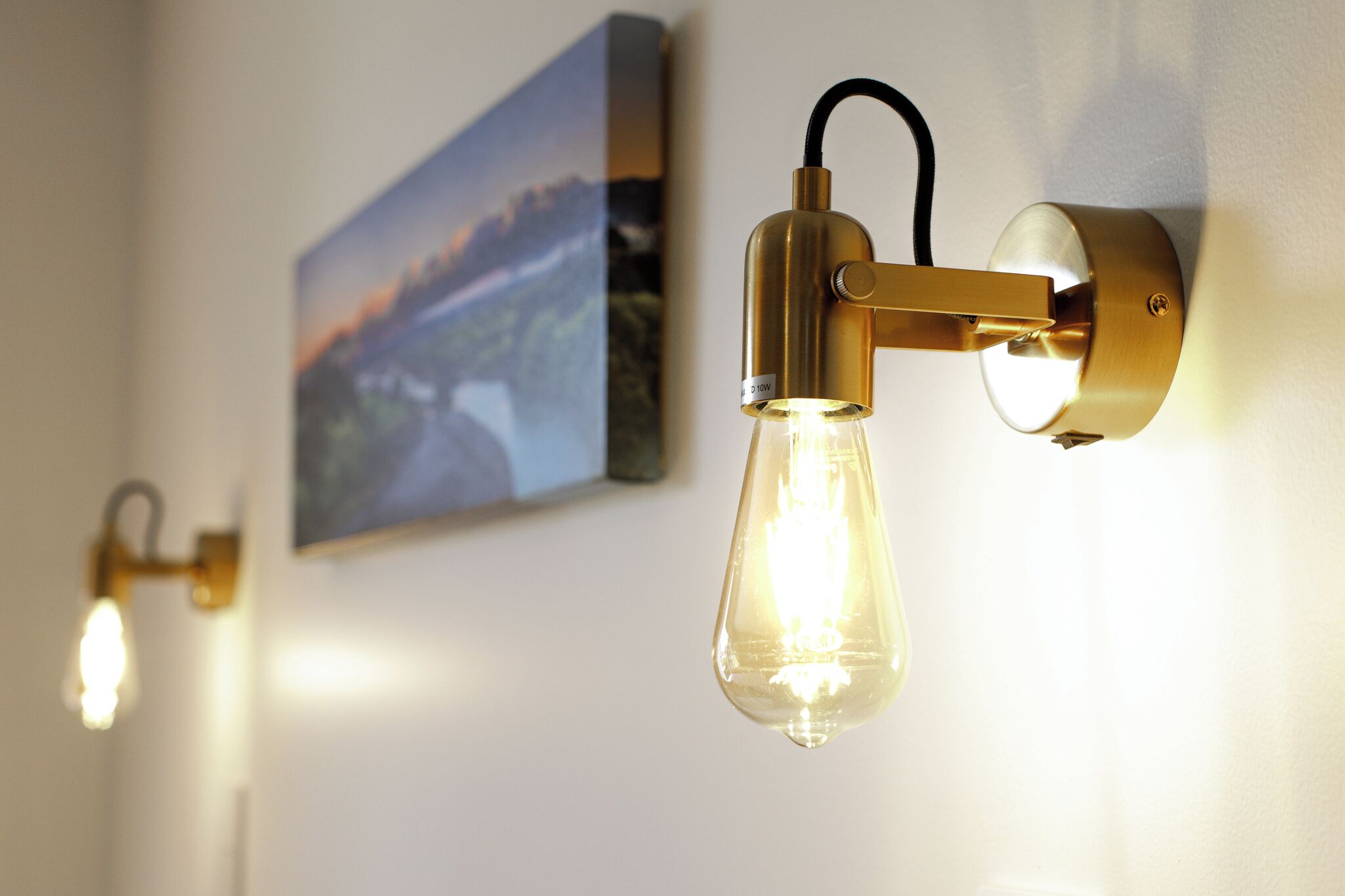 A wall-mounted light fixture with a clear glass bulb and a gold-colored base.