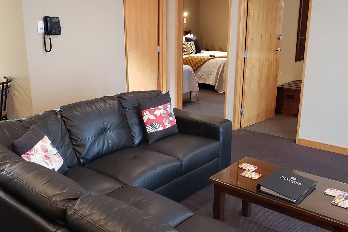 Una sala de estar con un sofá de cuero, una mesa de centro y una cama al fondo.