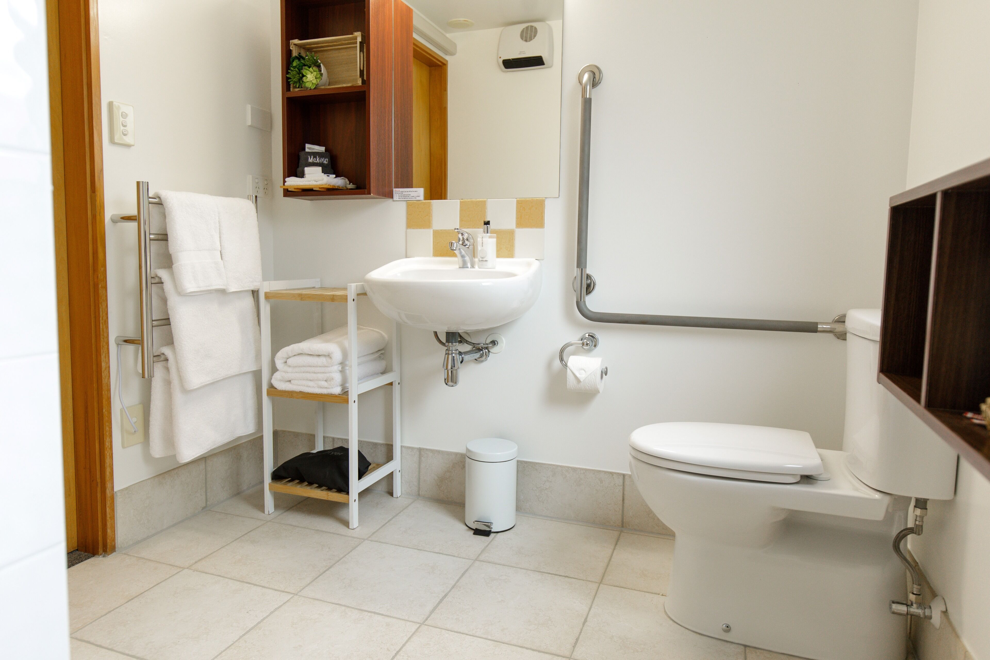 Un baño pequeño y limpio con un lavamanos, un inodoro y un pasamanos para facilitar el acceso.