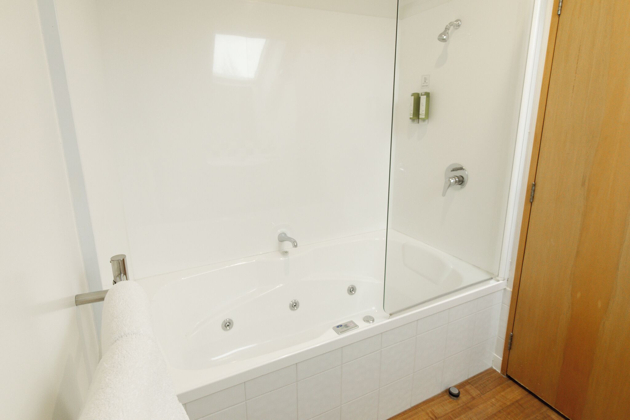 Un baño moderno con una bañera blanca, cabina de ducha de cristal y una puerta de madera.