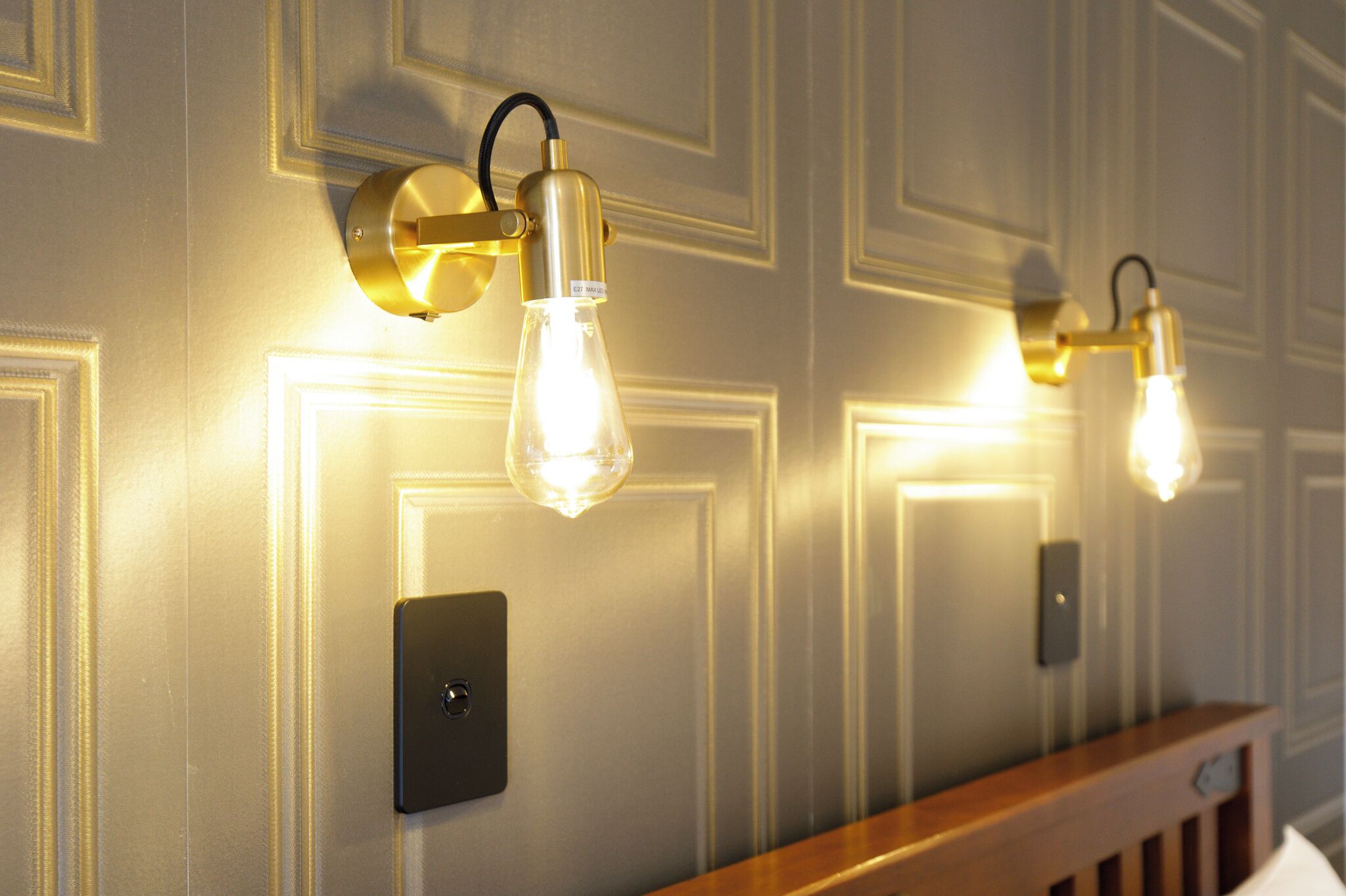 Wall-mounted light fixtures with exposed bulbs, a switch, and a wooden railing.