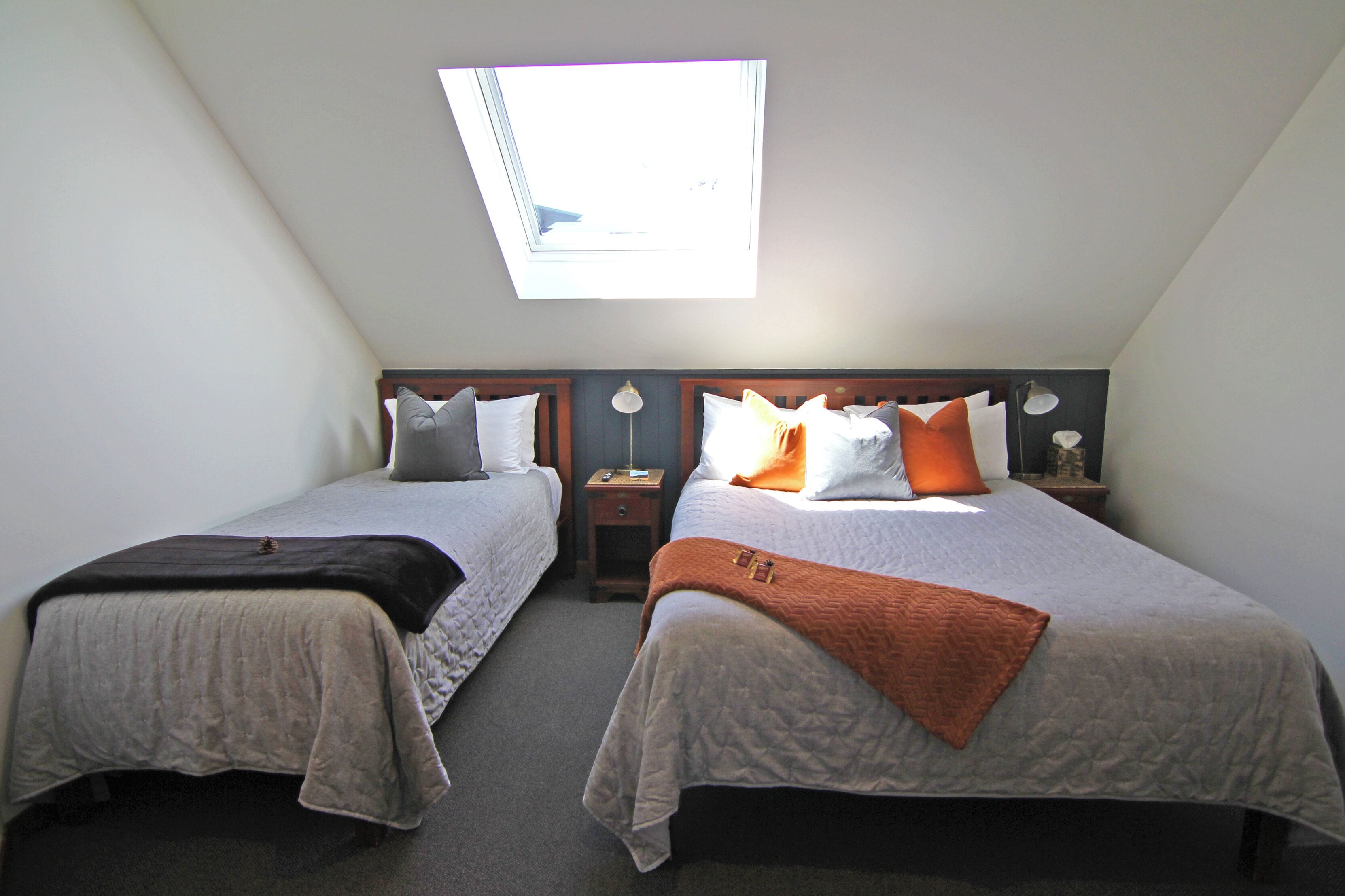 Une chambre avec deux lits, une lucarne et une petite table avec une lampe.