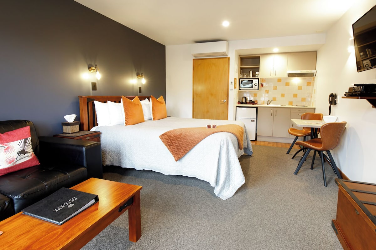 Una habitación de hotel con cama, escritorio, silla, sofá y una pequeña kitchenette.