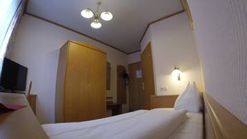 A compact hotel room with a single bed, a wooden wardrobe, a television, and a ceiling light fixture.