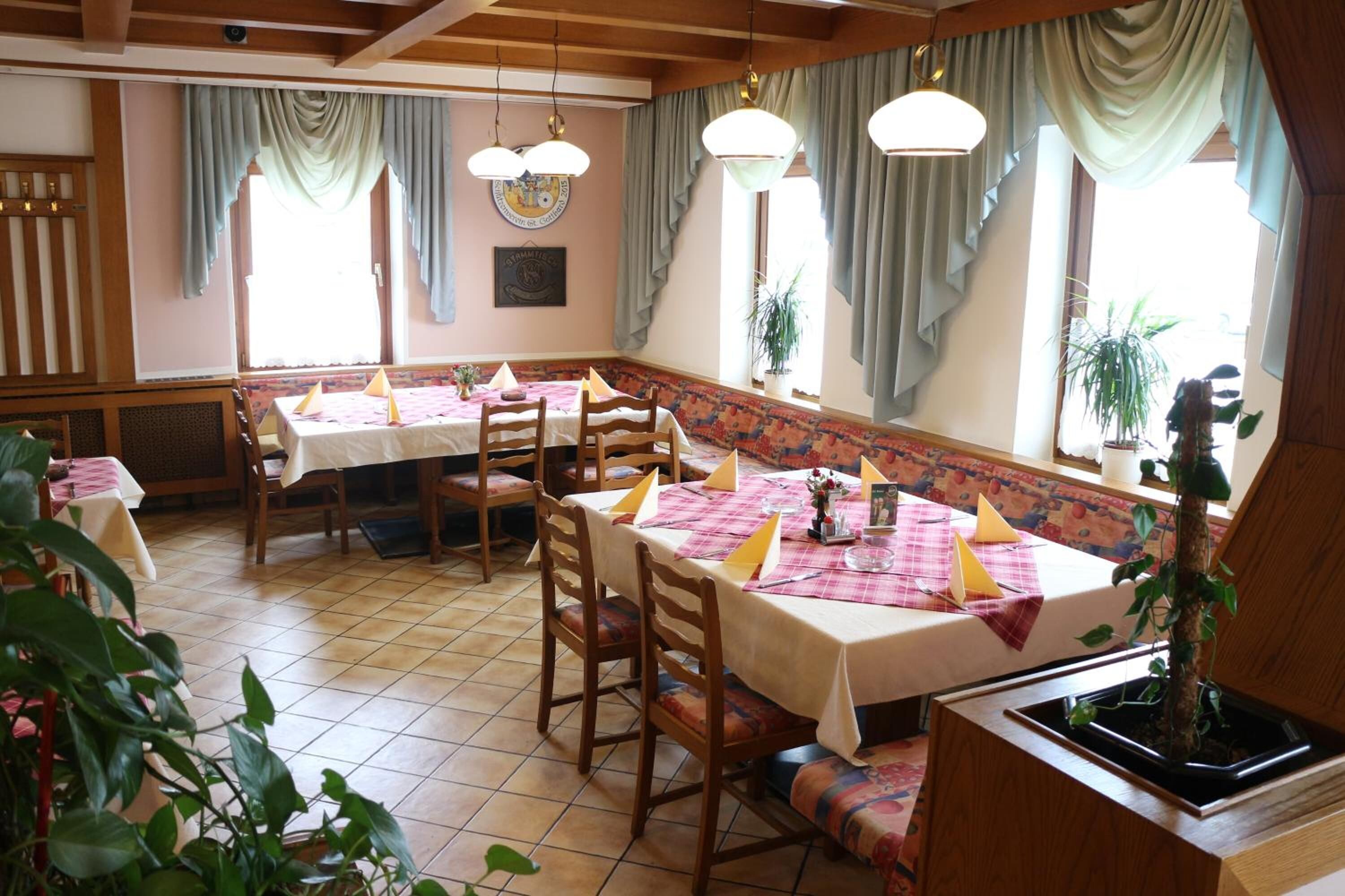 Un comedor con mesas y sillas de madera, un banco estampado y ventanas grandes con cortinas.