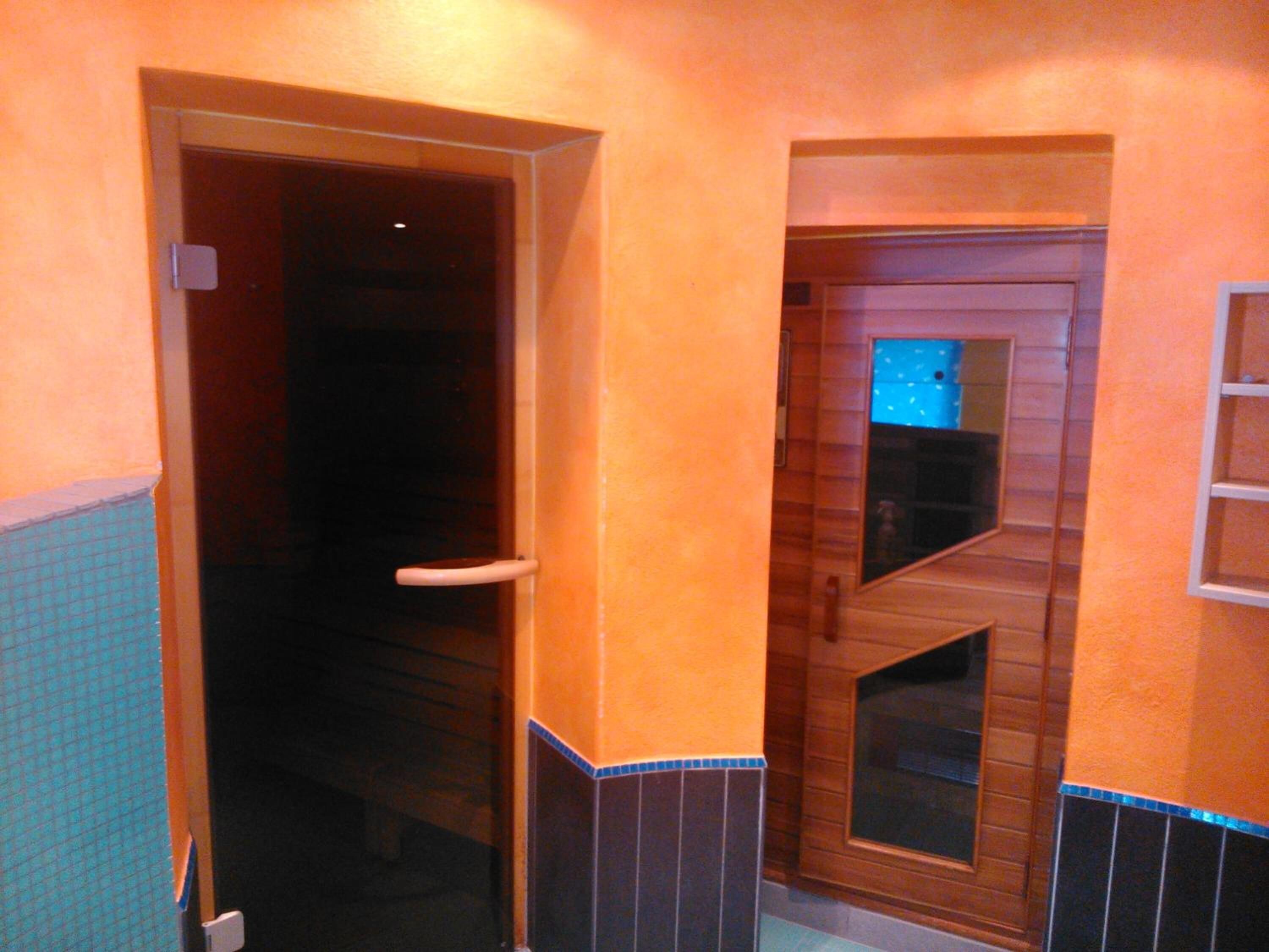 Un baño con puerta de madera, un espejo y pared con azulejos.