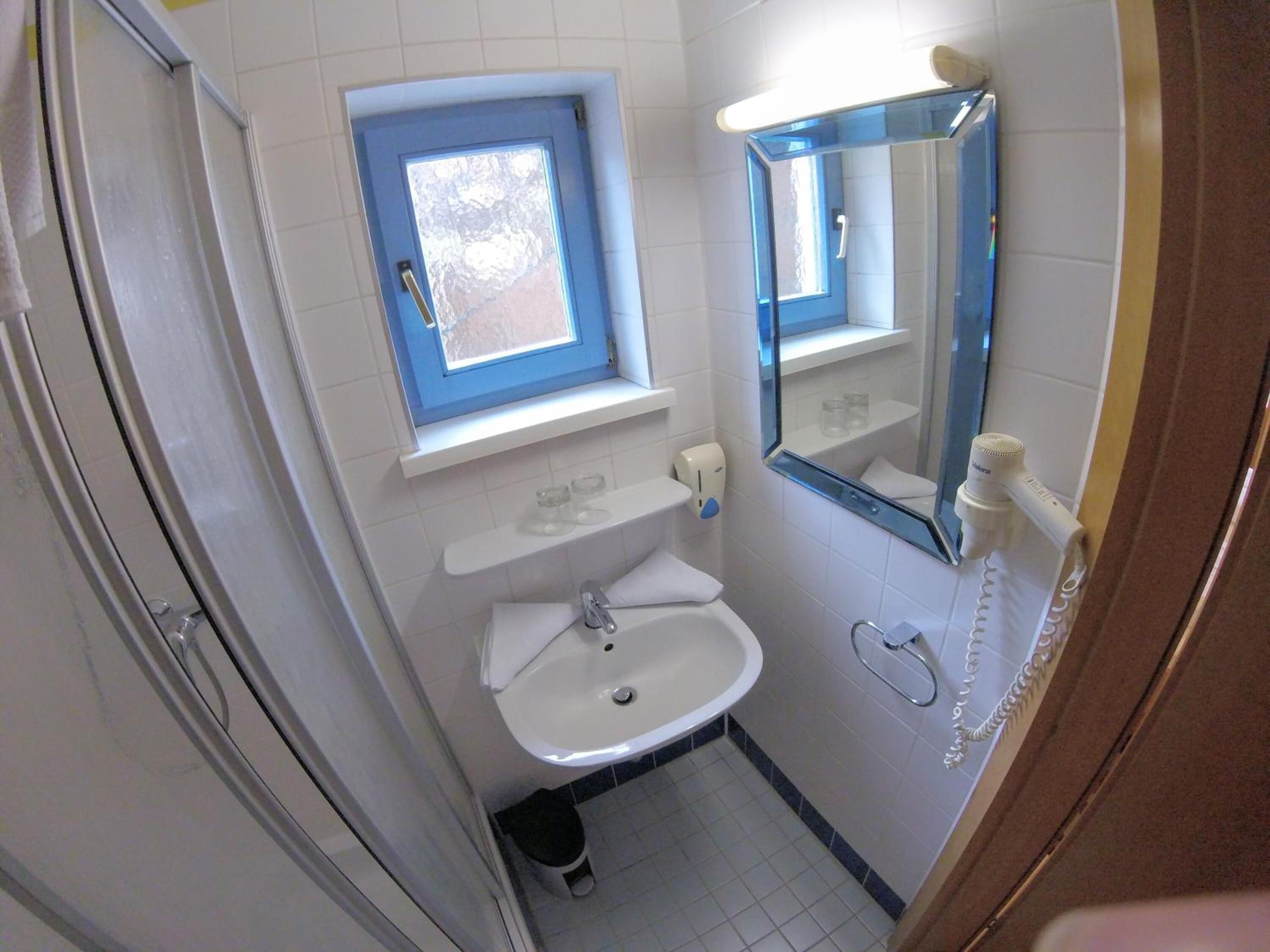 Ein kleines Badezimmer mit Fenster, Waschbecken, Spiegel und Toilette.