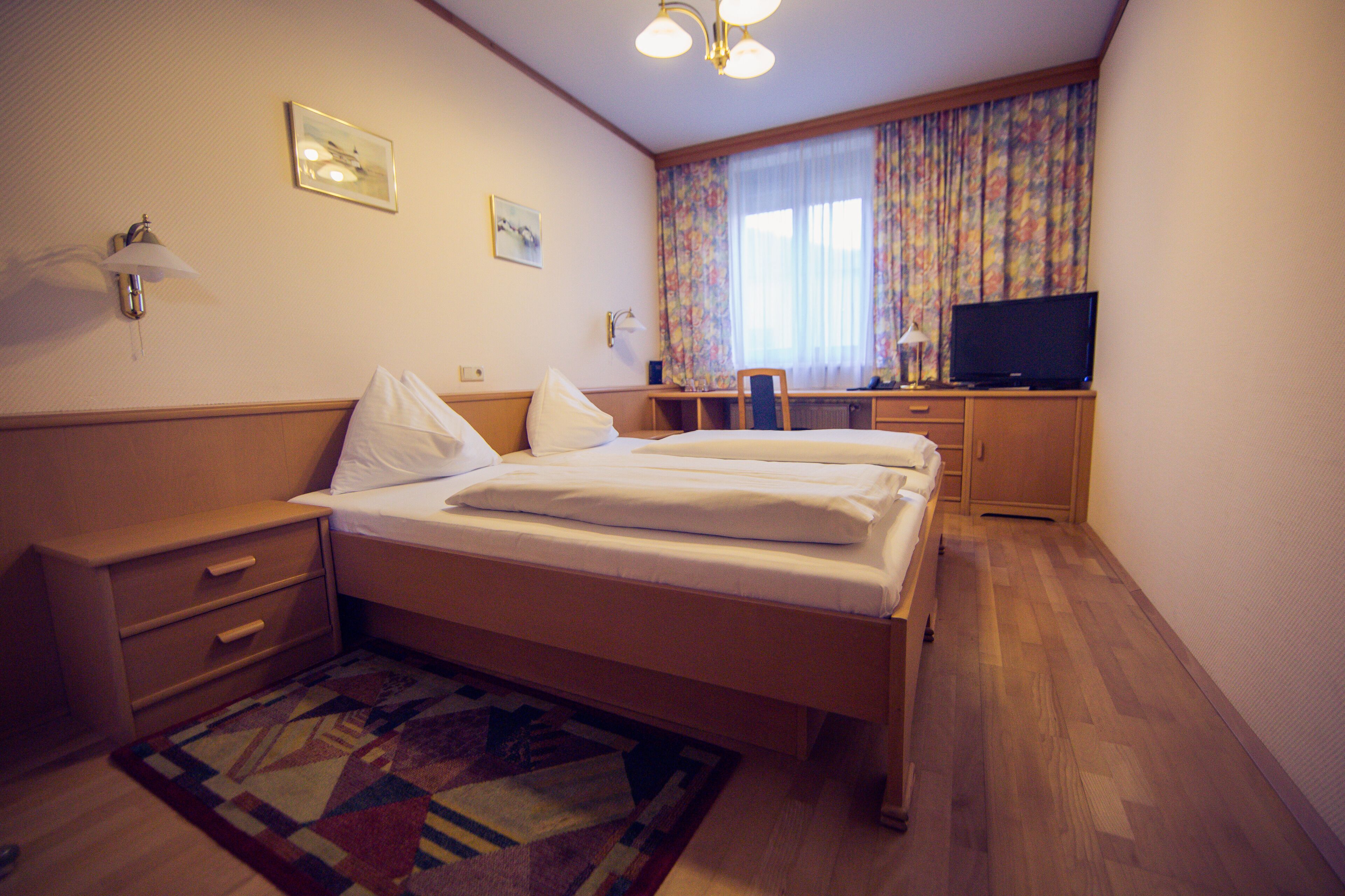 Una habitación de hotel con cama, escritorio, televisor y ventana con cortinas.