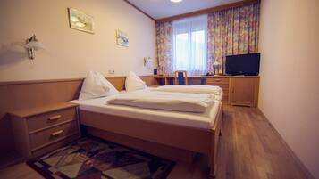 Una habitación de hotel con cama, escritorio, televisor y ventana con cortinas.