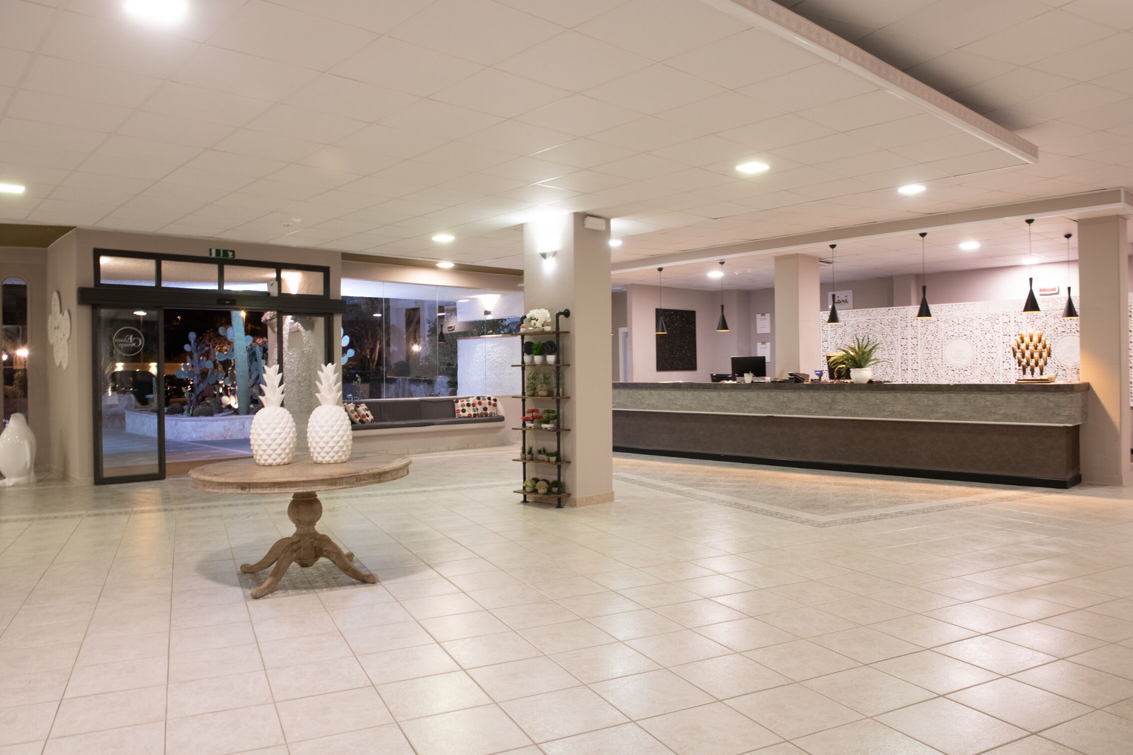 Hall moderna di un hotel con una reception, un tavolo rotondo con oggetti decorativi e un'ampia finestra.