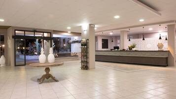Hall moderna di un hotel con una reception, un tavolo rotondo con oggetti decorativi e un'ampia finestra.