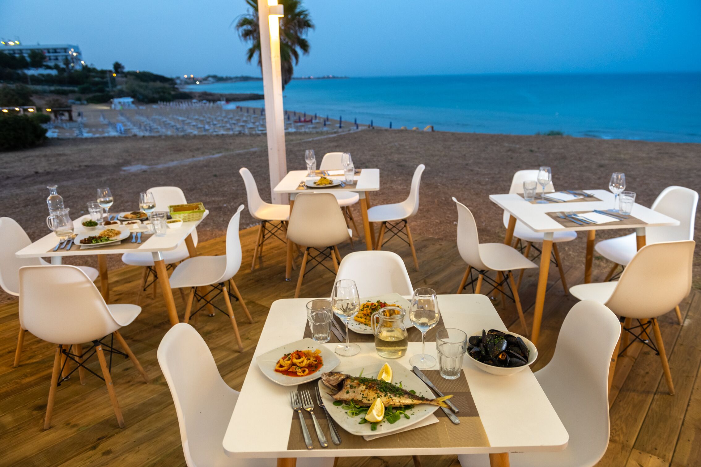 A seaside restaurant with tables set for dining, overlooking the beach and ocean.