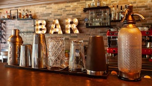 A bar area with a brick wall, shelves with bottles, and a variety of bar tools on the counter.