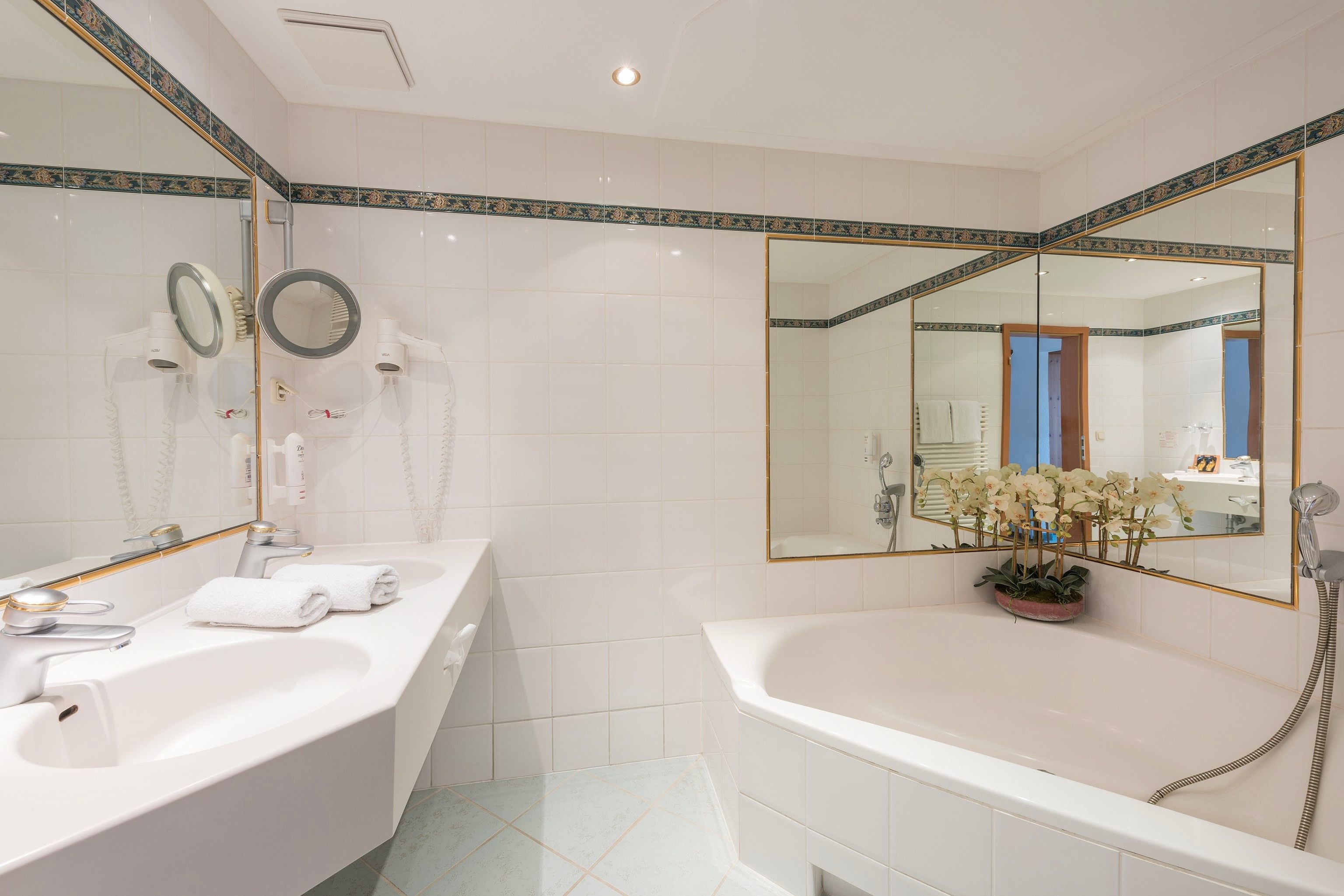 A bathroom with a white sink, two mirrors, a bathtub, and a potted plant.