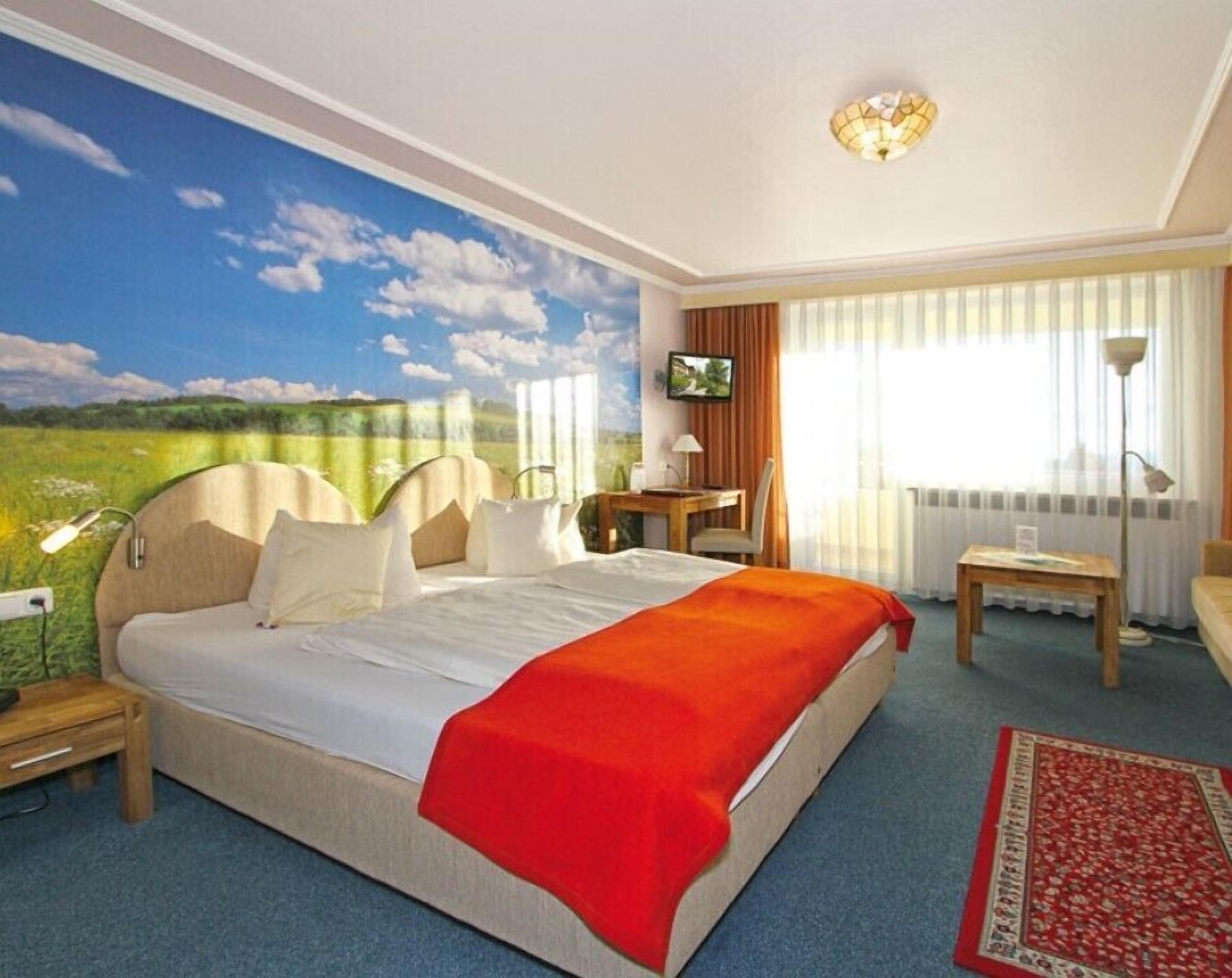 Ein Hotelzimmer mit einem großen Bett, einem Schreibtisch, einem Sessel, einem Fernseher und einem Fenster mit Vorhängen.