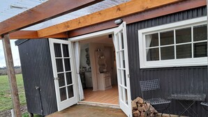 A wooden deck leading to a house with a large open door, a small outdoor table, and a stack of firewood.