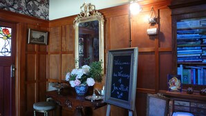 A room with wooden paneled walls, a large mirror, a chalkboard with a welcome message, a vase of flowers, and a bookshelf filled with books.