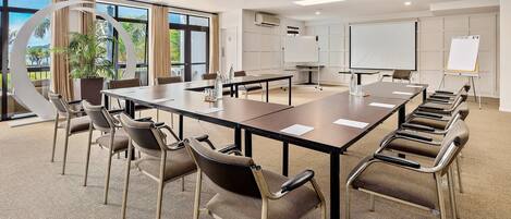 A conference room with a long table, chairs, a whiteboard, and a projection screen.