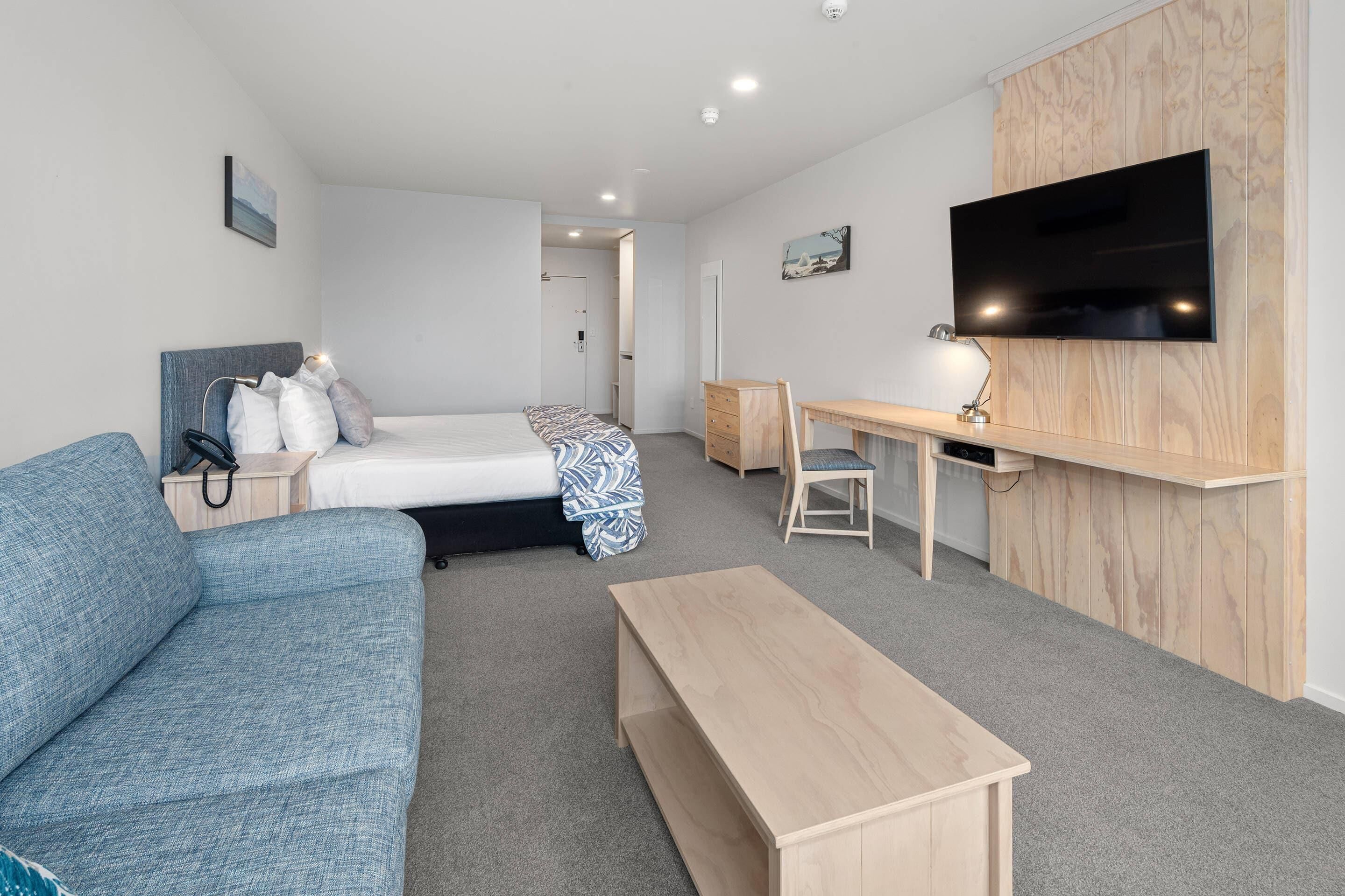A hotel room with a bed, a sofa, a desk, a TV, and a wooden panel wall.