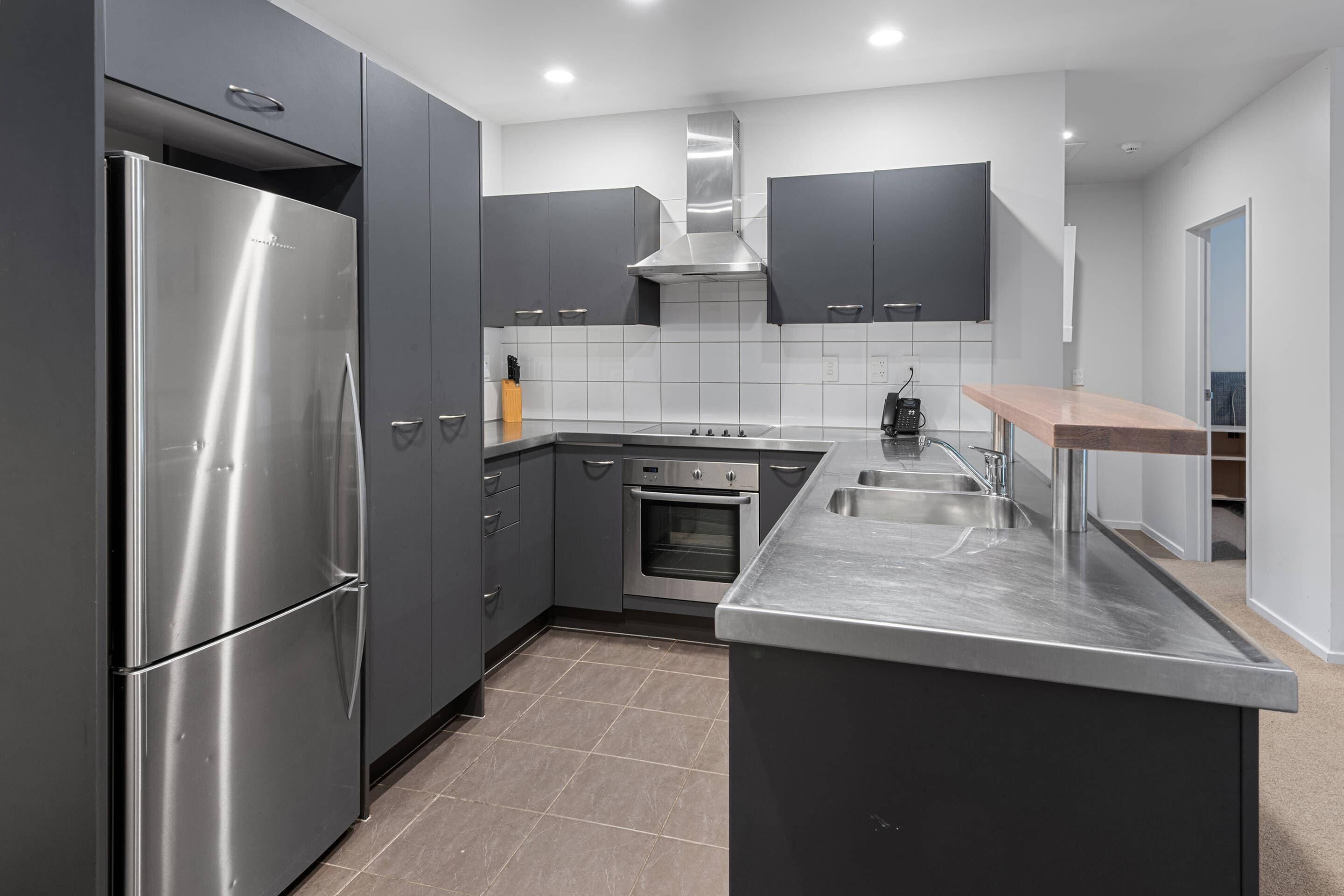 Una cocina moderna con gabinetes oscuros, electrodomésticos de acero inoxidable, horno empotrado y una isla grande con pileta.