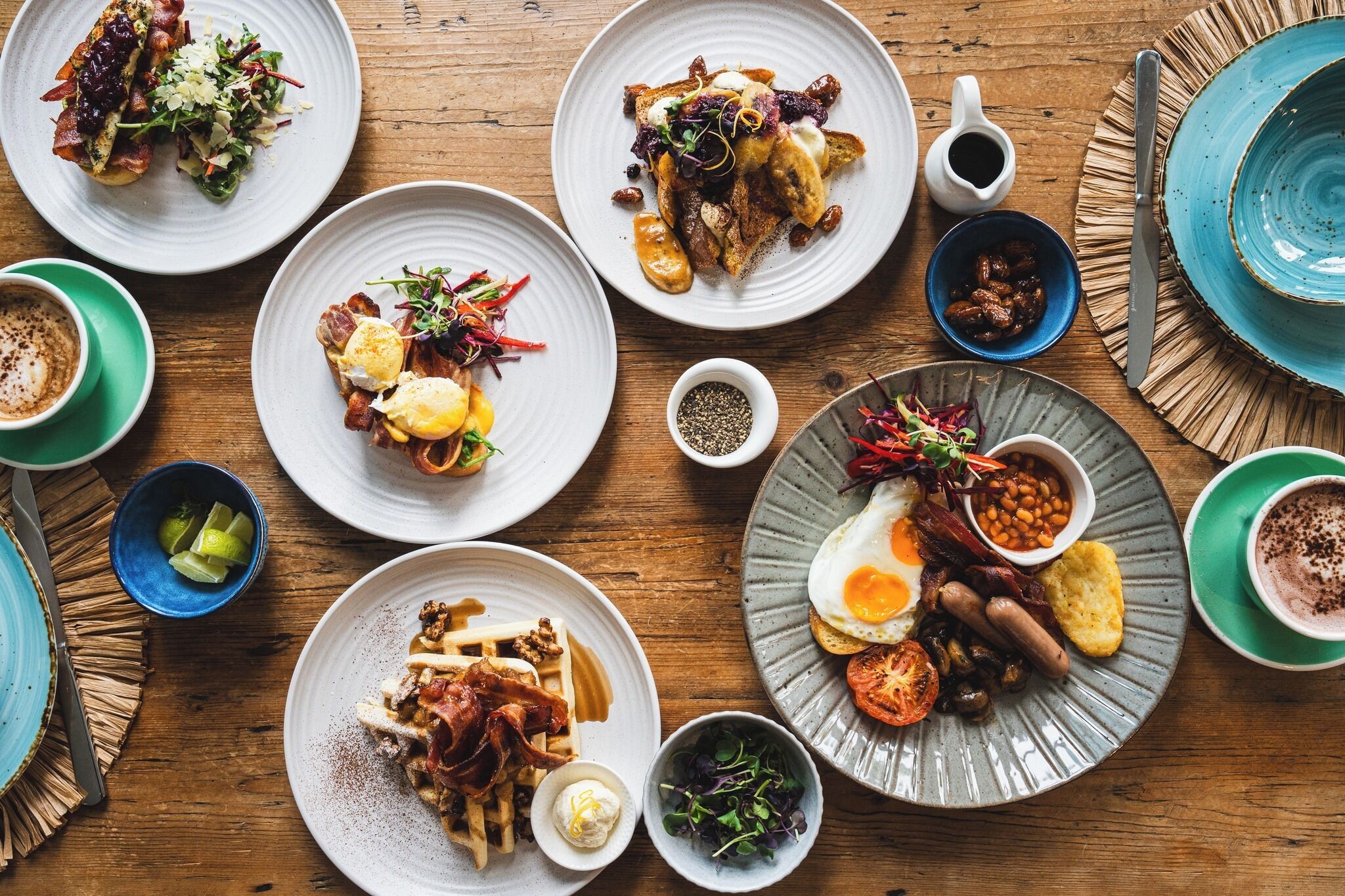 A variety of breakfast dishes on plates, including eggs, bacon, and toast, arranged on a wooden table.