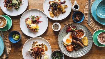 Diverse ontbijtgerechten op borden, zoals eieren, spek en toast, gerangschikt op een houten tafel.